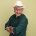 pleased middle-aged man wearing green t-shirt and hat crossing hands isolated on olive green background pleased middle-aged man wearing green t-shirt and hat crossing hands isolated on olive green background