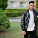 Stylish indian beard man at black leather jacket. India model po Stylish indian beard man at black leather jacket. India model posed at green garden of city.